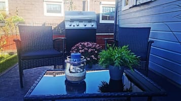 Een terras met een barbecue, tuinmeubilair en een bloempot.