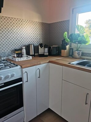 A compact kitchen with white cabinets, a gas stove, a coffee maker, and a potted plant.