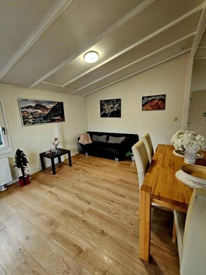 A living room with a wooden dining table, a black sofa, and a small side table.