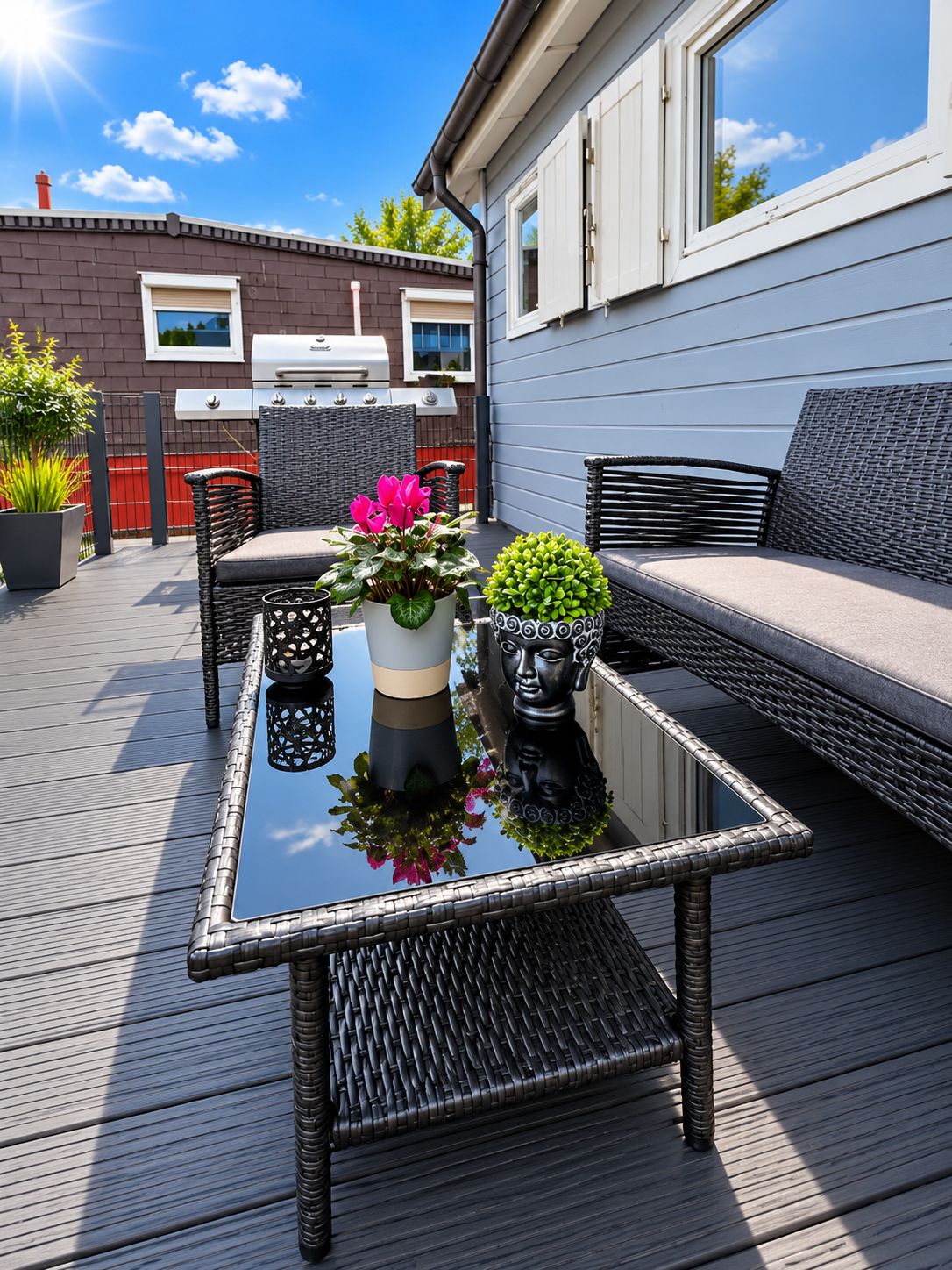 Eine Terrasse mit Gartenmöbeln, einem Grill und Topfpflanzen.