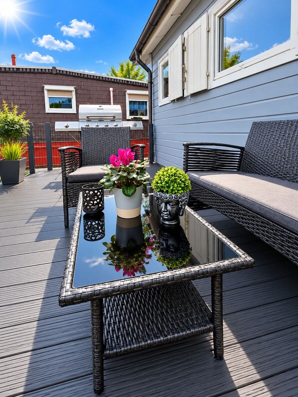 A deck with outdoor furniture, a grill, and potted plants.