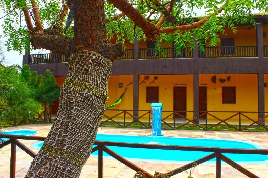 Un árbol cubierto con una red, una piscina azul y un edificio con balcones.