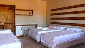 Habitación de hotel con tres camas, un refrigerador pequeño, cabecera de madera y estante en la pared.
