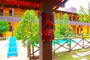 A building with a pool, a blue slide, and a wooden structure with a carved face.