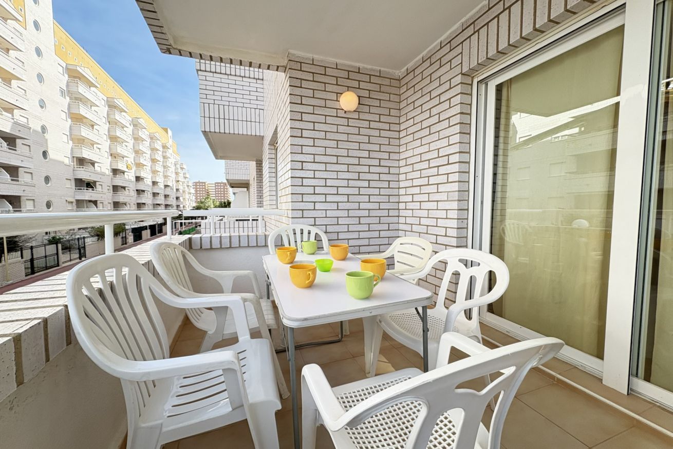 A balcony with white plastic chairs and a table, a glass door, and a brick wall.