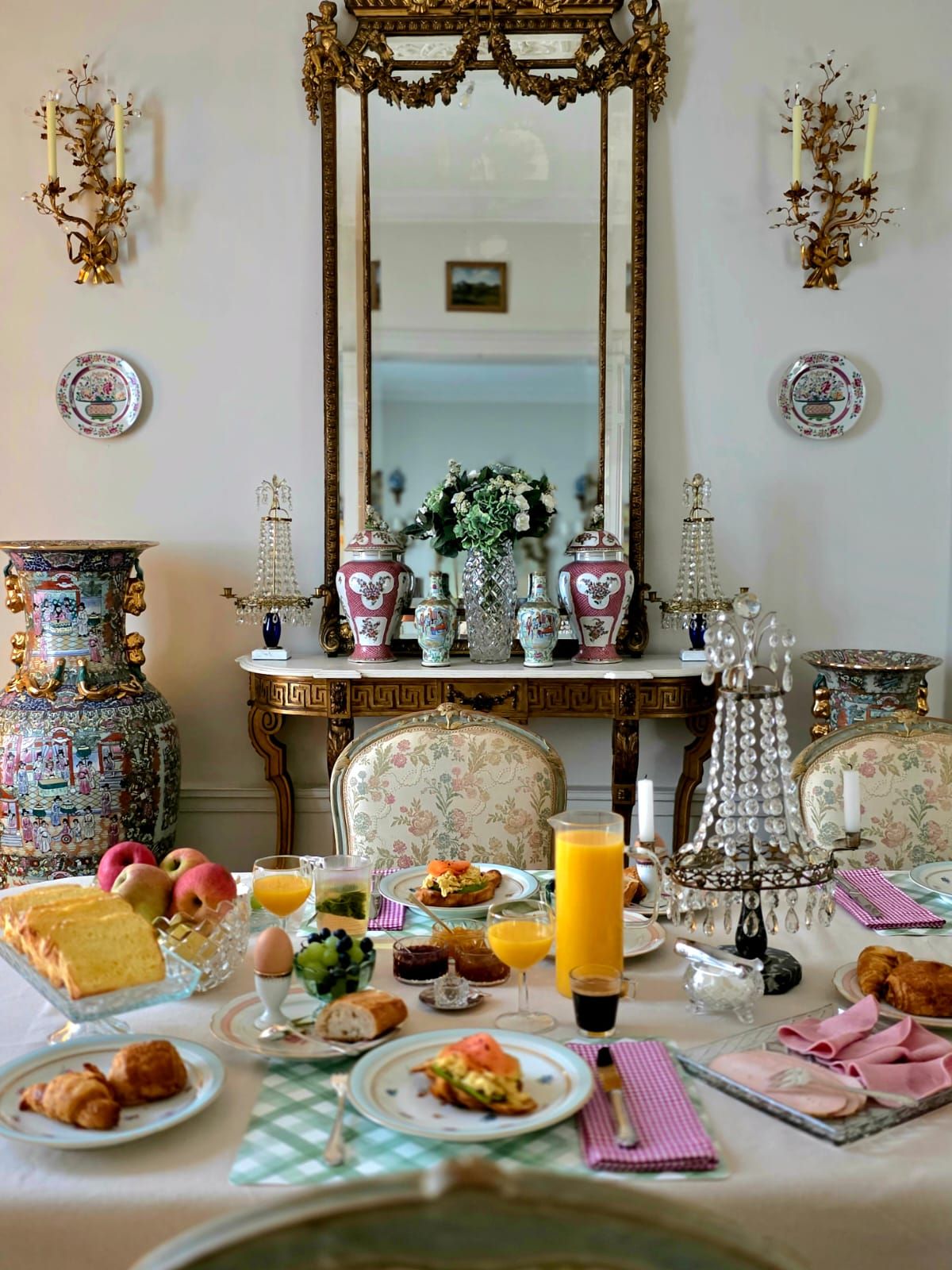 A dining table set with various dishes, a mirror, decorative vases, and wall sconces.