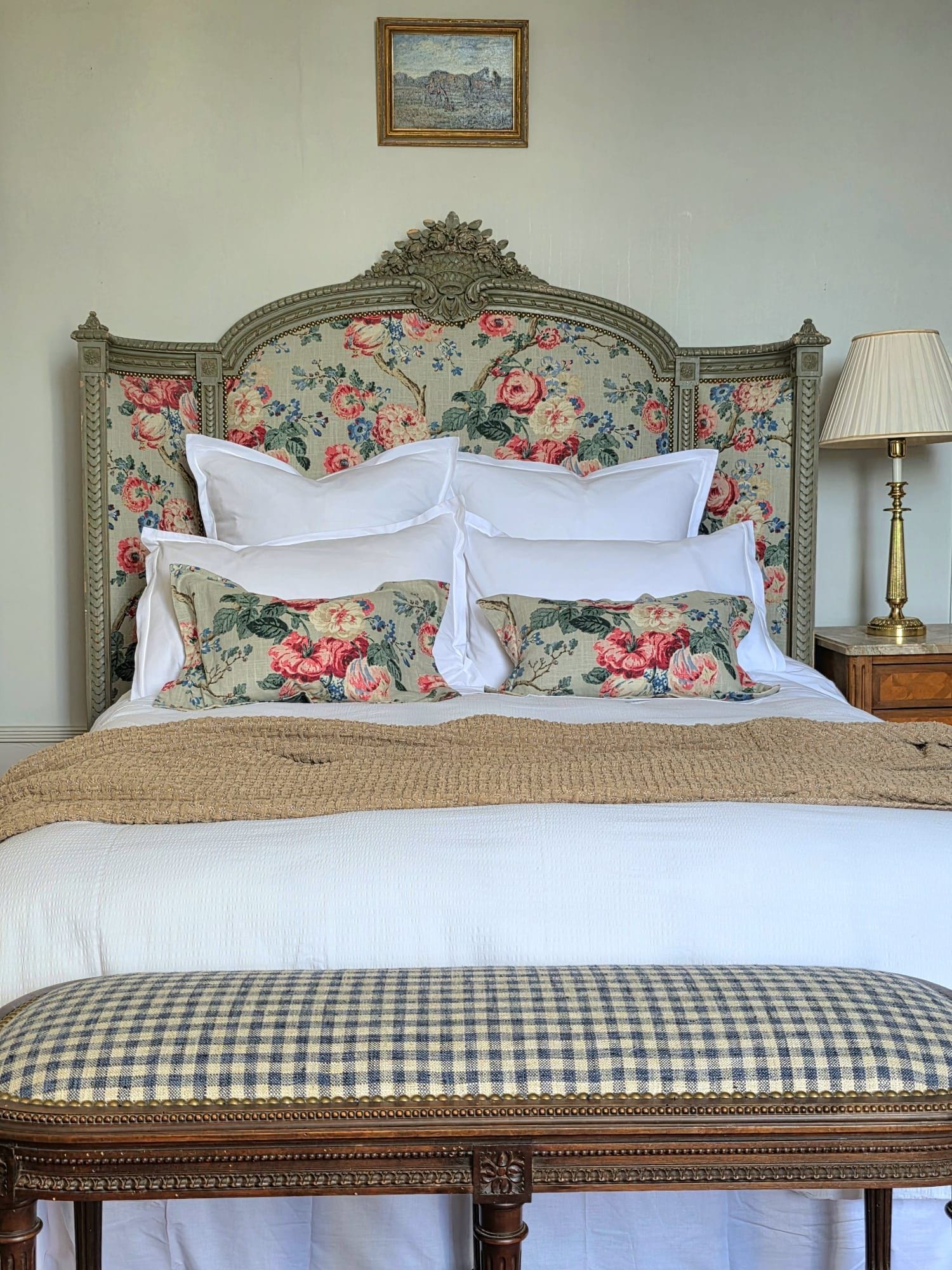 A bed with floral headboard, white pillows, and a checkered bench.