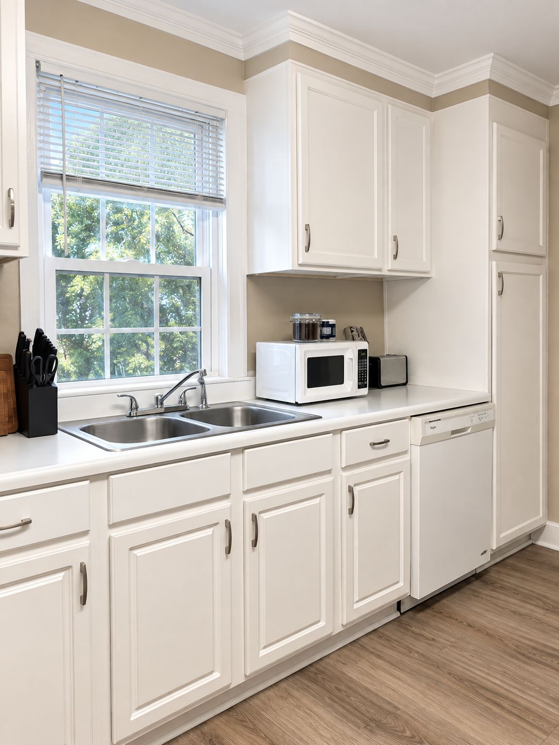 A kitchen with white cabinets, a double sink, a microwave, and a dishwasher.