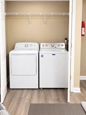 A laundry room with two white Maytag washers and dryers, a white door, and a beige wall.