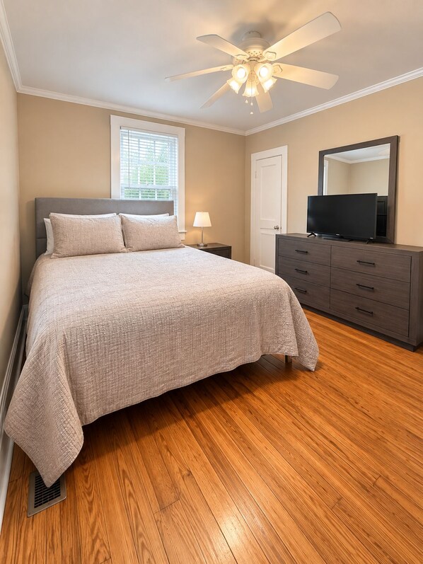 A bedroom with a bed, a dresser, a television, a ceiling fan, and a window.