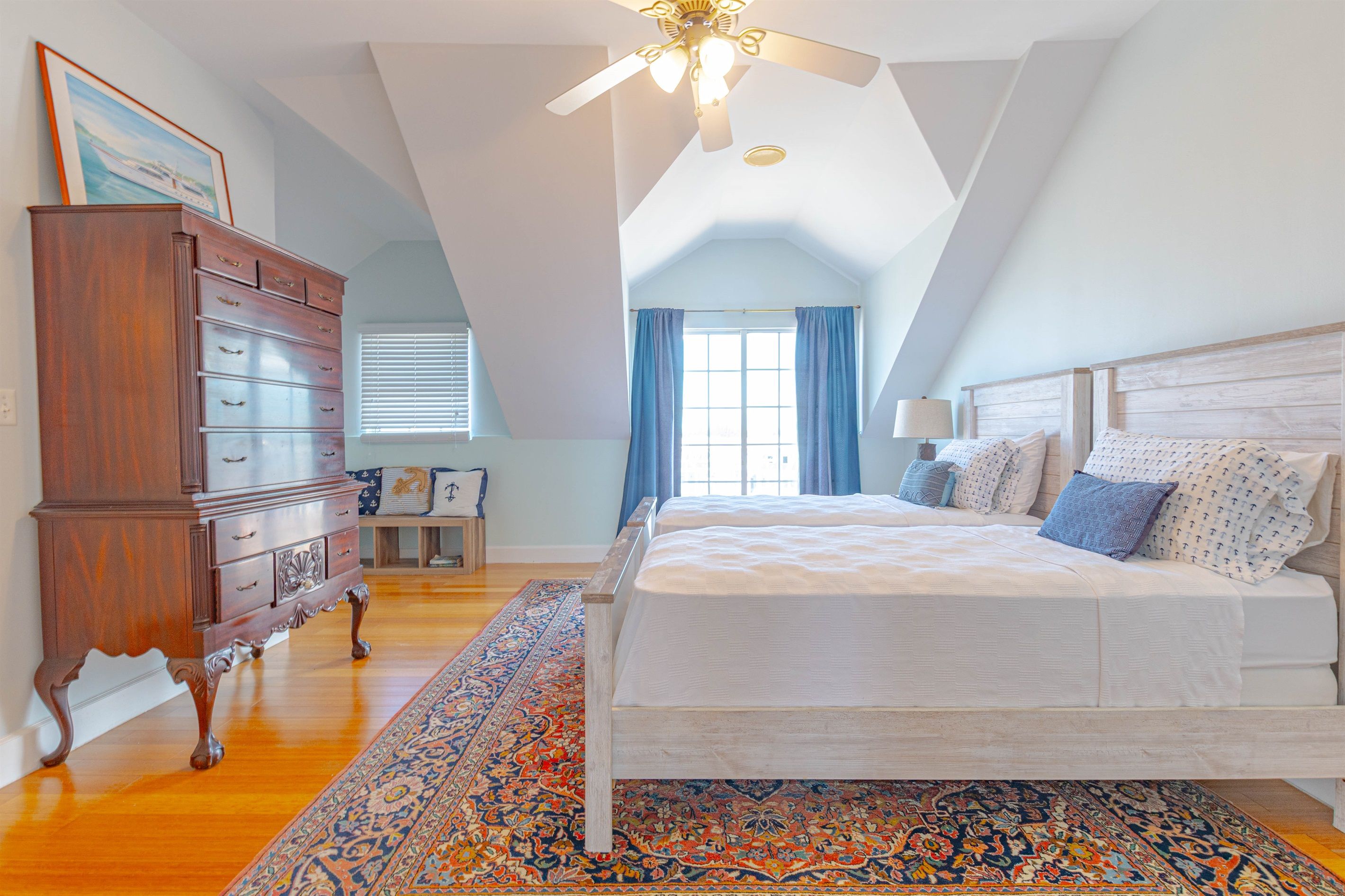 A bedroom with a large bed, a dresser, a ceiling fan, and a window with curtains.