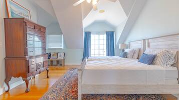 A bedroom with a large bed, a dresser, a ceiling fan, and a window with curtains.