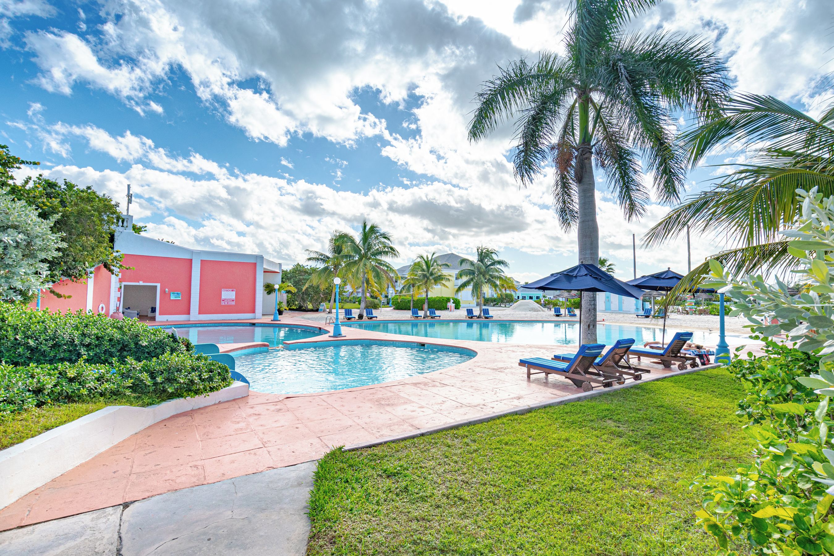 A pool area with a red building, palm trees, and lounge chairs.