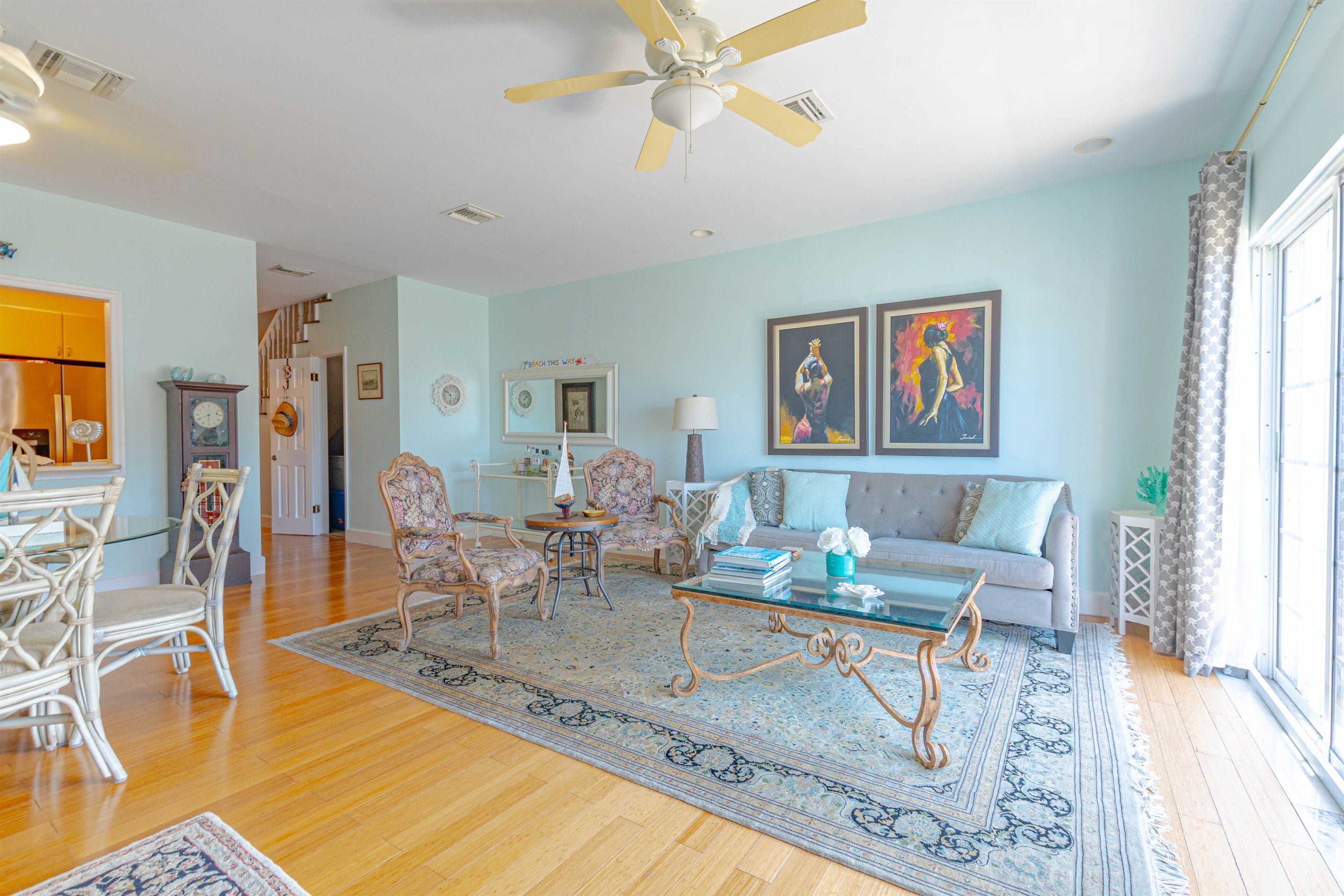 A spacious living room with a wooden floor, a glass coffee table, a sofa, and a ceiling fan.