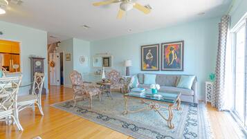 A spacious living room with a wooden floor, a glass coffee table, a sofa, and a ceiling fan.