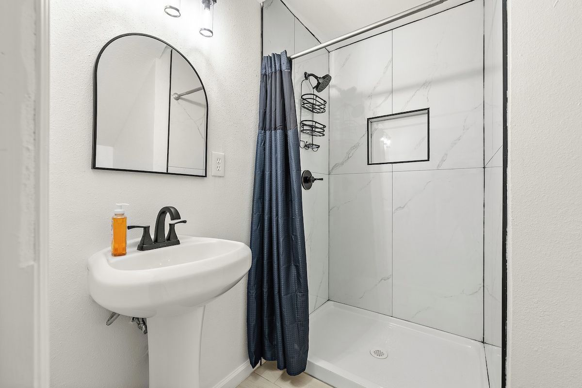 A bathroom with a white sink, a mirror, and a shower area with a glass door.