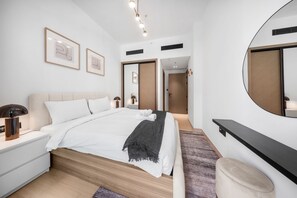 A modern bedroom with a large bed, bedside lamps, a bedside table, a mirror, and a wardrobe. - Stayshort - Peace and Tranquility in This 1 Bedroom in JVC (Dubai)
