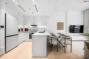 A modern kitchen with white cabinetry, a central island, and a dining area with chairs and a table. - Stayshort - Peace and Tranquility in This 1 Bedroom in JVC (Dubai)