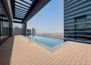 A rooftop infinity pool with a wooden deck, surrounded by modern buildings and a clear sky. - Stayshort - Chic 1 Bedroom Unit in Dubai Marina That Sleeps 4 (Dubai)