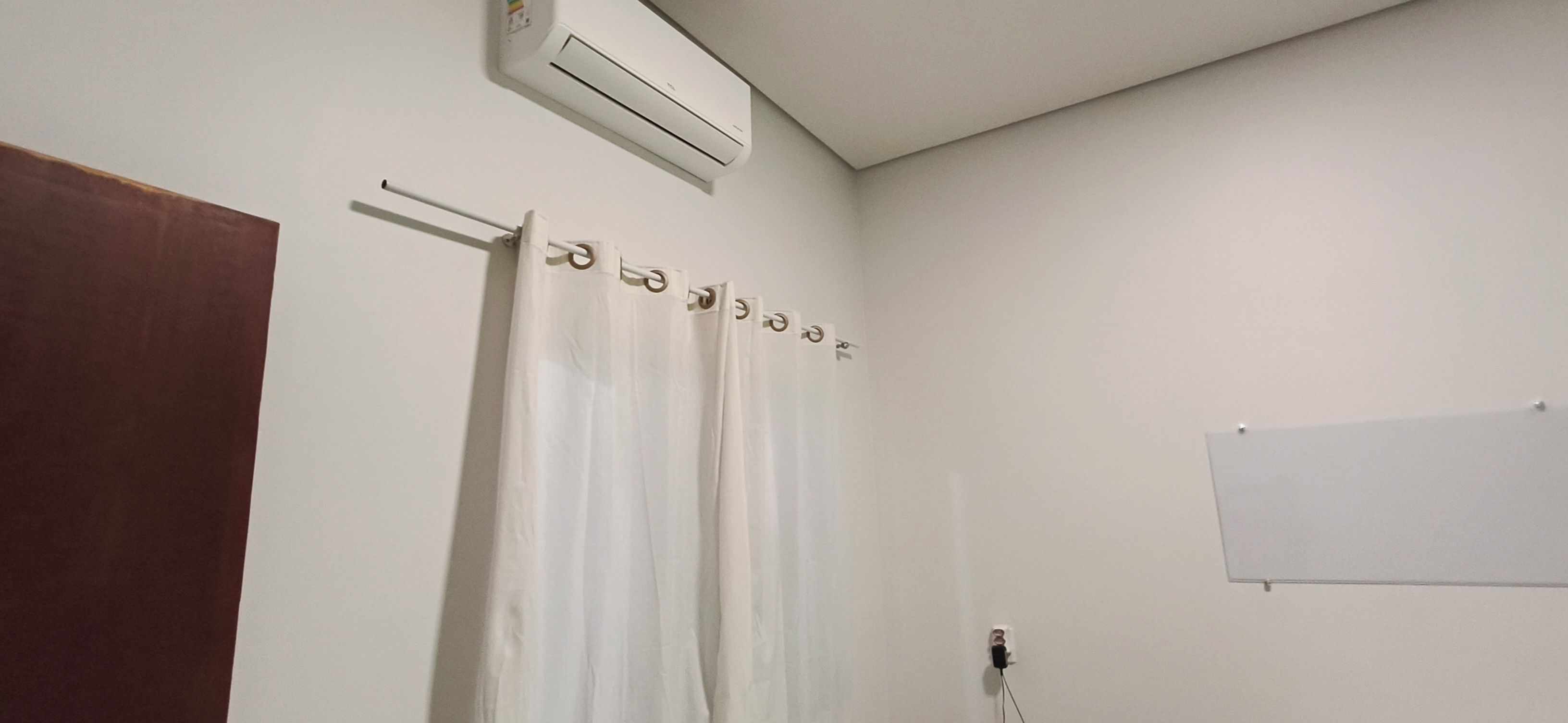 A bathroom with a white shower curtain, a towel rack, a whiteboard, and an air conditioning unit.