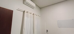 Ett badrum med ett vitt duschdraperi, en handduksställning, en whiteboard och en luftkonditioneringsanläggning.