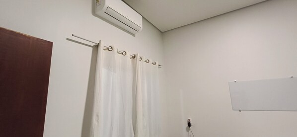 A bathroom with a white shower curtain, a towel rack, a whiteboard, and an air conditioning unit.