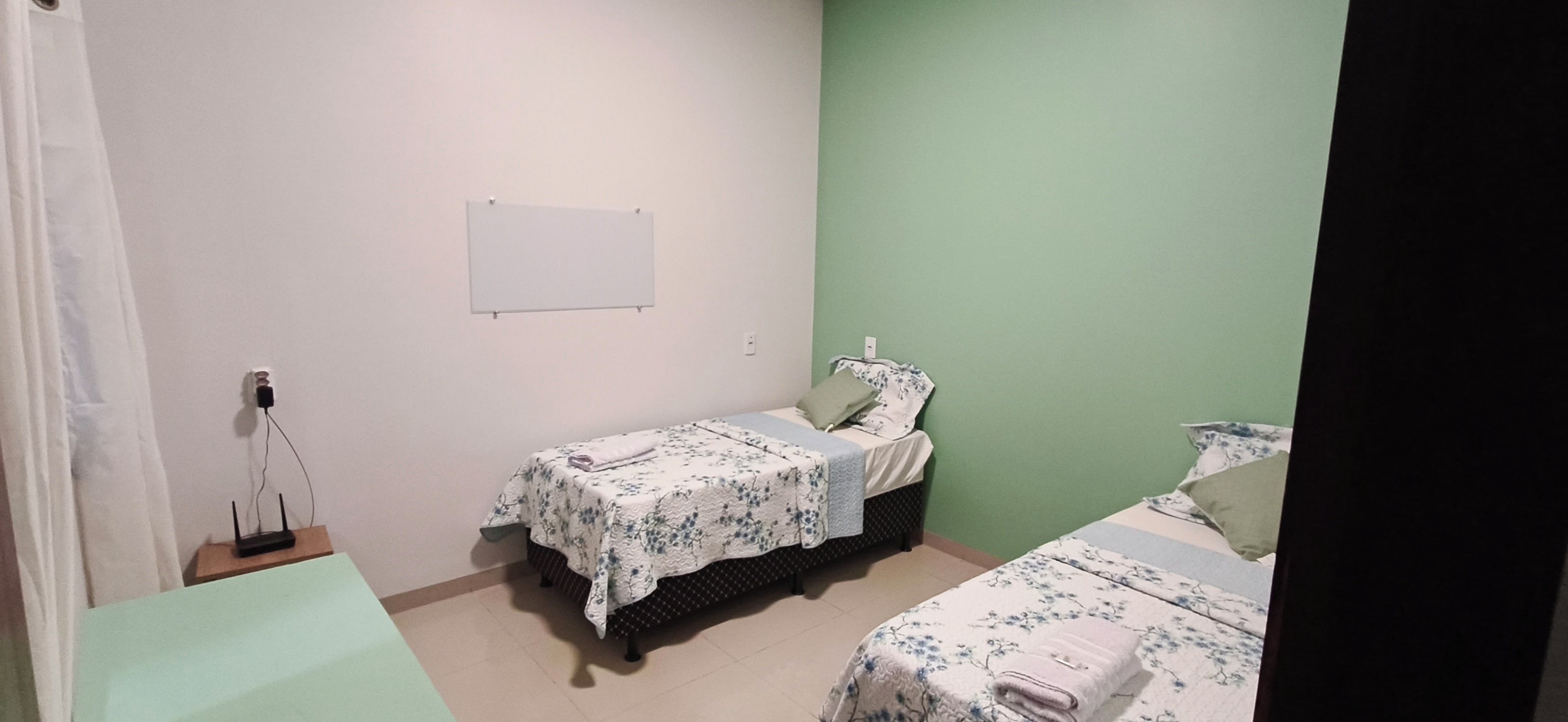 A small, clean room with two single beds, a whiteboard on the wall, and a power outlet with a charger.