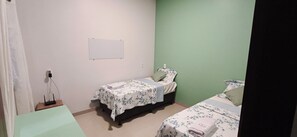 A small, clean room with two single beds, a whiteboard on the wall, and a power outlet with a charger.
