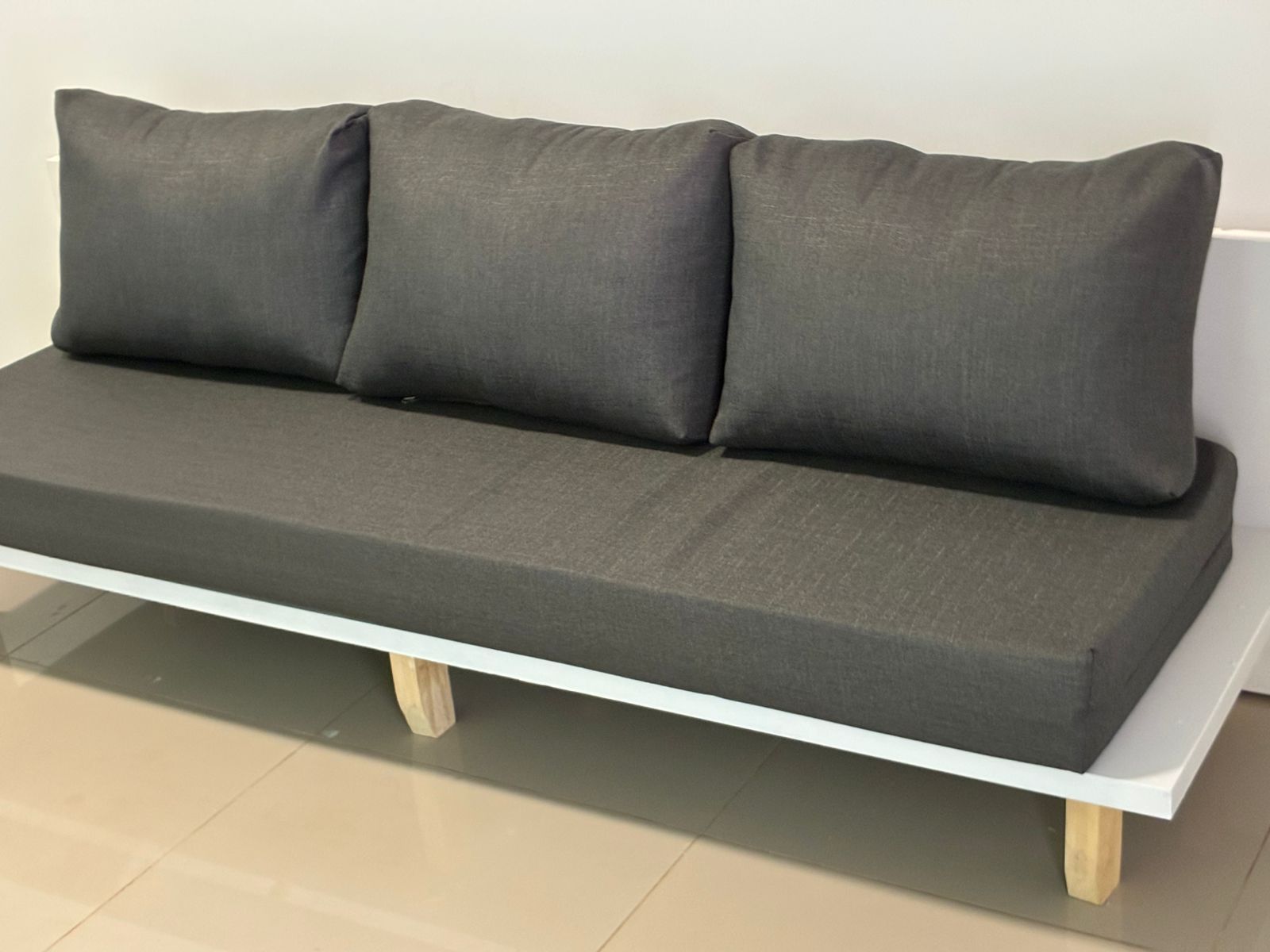 Un canapé moderne avec une structure blanche et des pieds en bois, placé contre un mur uni.