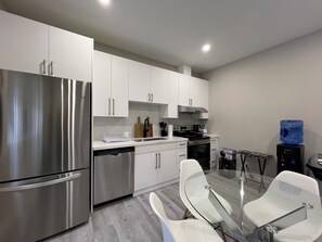 A modern kitchen with stainless steel appliances, white cabinetry, and a glass dining table. - Room +Private Bath in New Windsor House (Windsor)