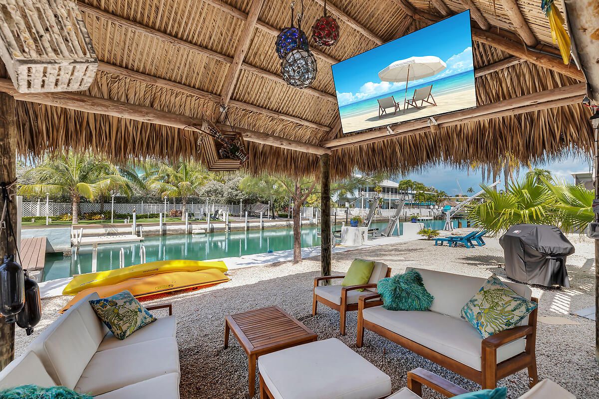 A covered outdoor seating area with a pool, lounge chairs, and a beach scene on the wall.