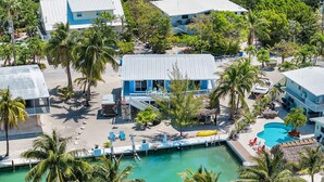 An aerial view of a resort with a pool, palm trees, and a blue building with outdoor seating. - Islamorada studio suite — queen bed, no kitchen (Islamorada)