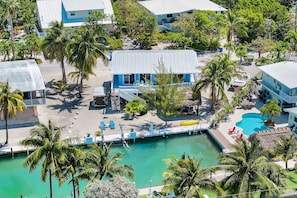 Ett flygbildsfoto av ett semesterområde med en pool, palmer och en blå byggnad med utomhusservering.