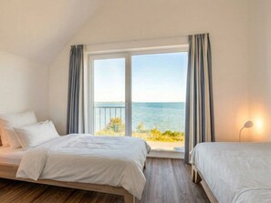 A bedroom with two beds, a large window with curtains, and a view of the sea. - Holiday Apartment With 1 Bedroom (Kappeln)