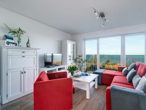 A modern living room with a television, red sofas, a white cabinet, and a large window with a view of the sea. - Holiday Apartment With 1 Bedroom (Kappeln)