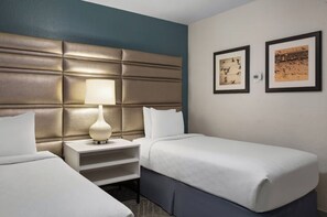 A hotel room with a large padded headboard, a bedside table with a lamp, two beds, and two framed pictures on the wall. - BLOCK Blue Ridge Village 2br (Banner Elk)
