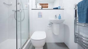A modern bathroom with a glass shower enclosure, a white toilet, a sink with a mirror above, and a towel rack. - Student Only The Gillows (Lancaster)