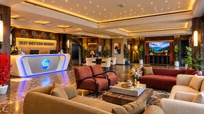 Un vestíbulo de hotel con mostrador de recepción, zona de estar y una pantalla grande.