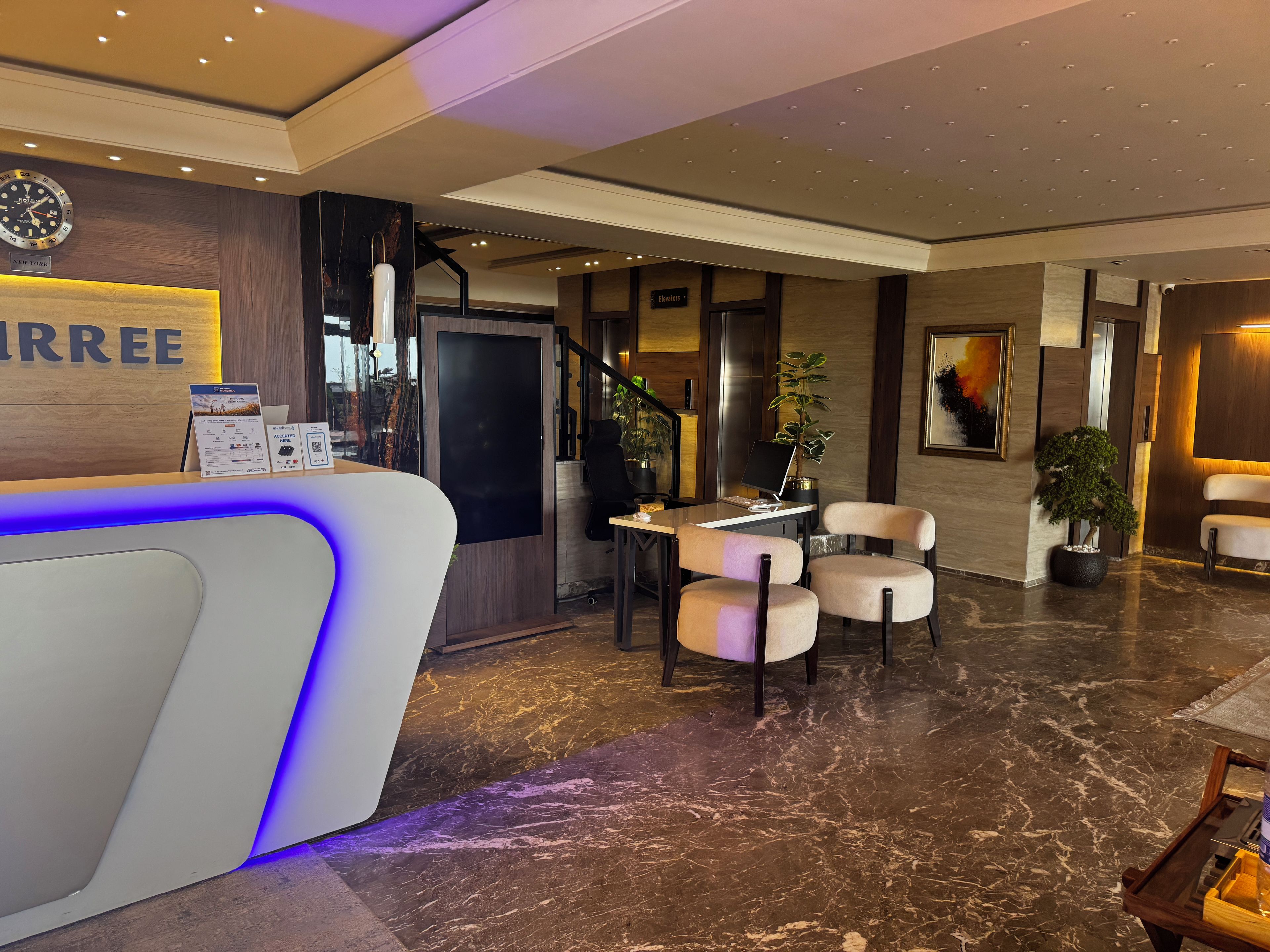 A hotel reception area with a reception desk, seating area, and a staircase.