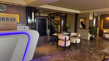 A hotel reception area with a reception desk, seating area, and a staircase.