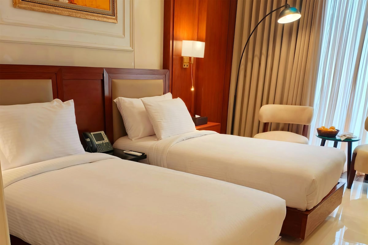 Habitación de hotel con dos camas, una mesita de noche con teléfono, una lámpara y una silla.
