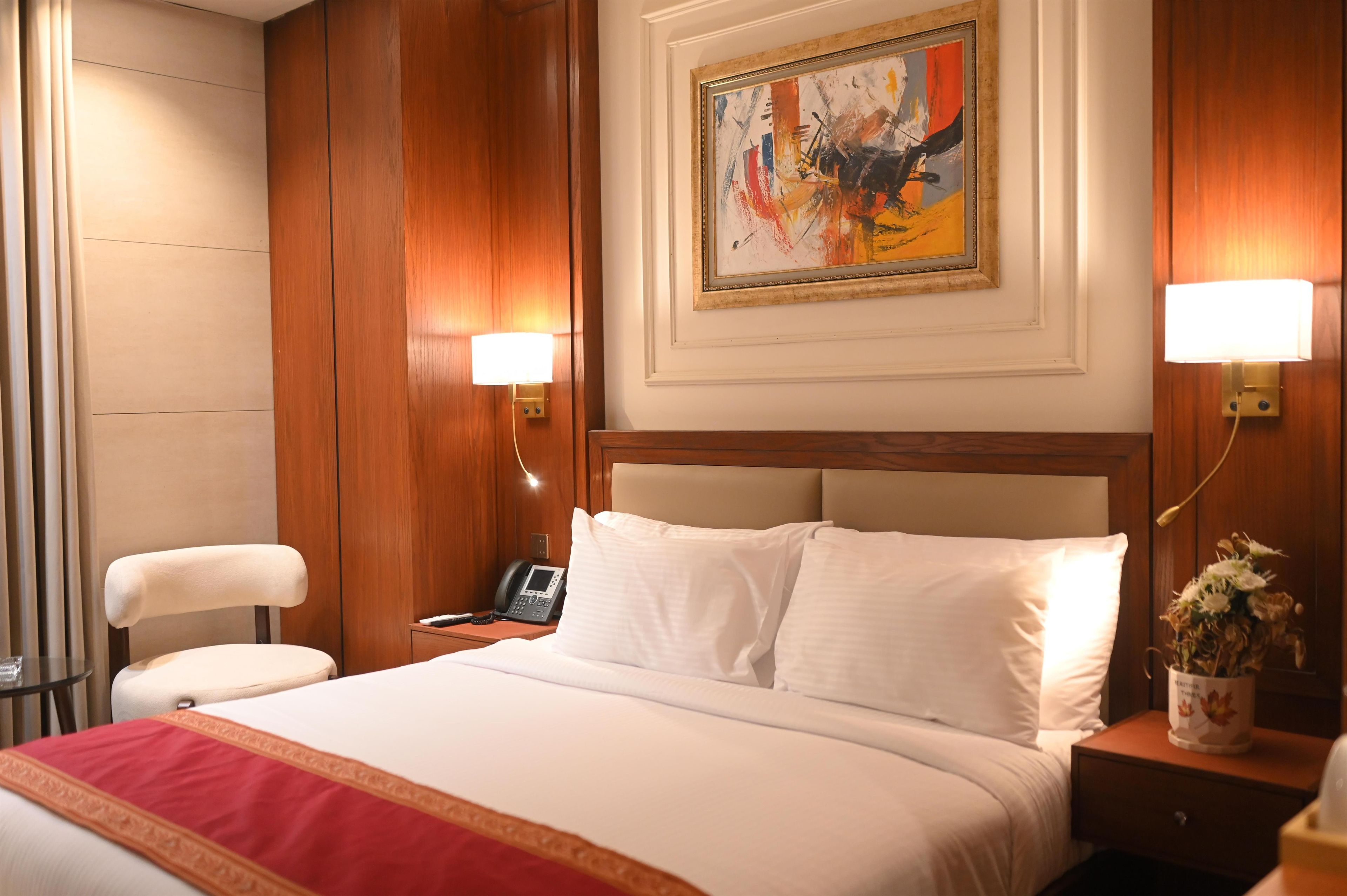 A hotel room with a large bed, a desk with a telephone, and a painting on the wall.