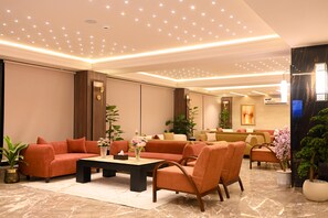 A modern hotel lobby with a seating area, a reception desk, and a large window.