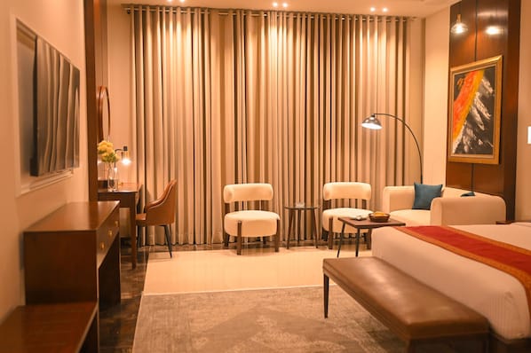 A hotel room with a bed, two armchairs, a sofa, a desk, and a lamp.