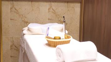 A neatly made bed with a white towel, a small basket, and a bottle, likely containing lotion or shampoo, in a room with a marble wall and wooden paneling.