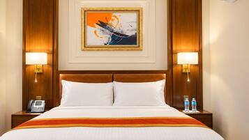 Une chambre d’hôtel avec un grand lit, deux lampes de chevet, un téléphone et une œuvre d’art encadrée au mur.