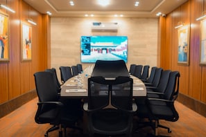 A conference room with a long table, black chairs, and a large screen at the front.