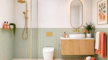 A bathroom with a white toilet, a wooden vanity with a sink, a shower with a gold showerhead, and a mirror with a gold frame.