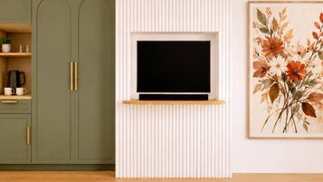 Ein Zimmer mit einem an der weißen Wand befestigten Fernseher, einem grünen Schrank mit Ablagefläche und einem gerahmten Blumenbild.