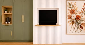 A room with a television mounted on a white wall, a green cabinet with a shelf, and a framed floral artwork.